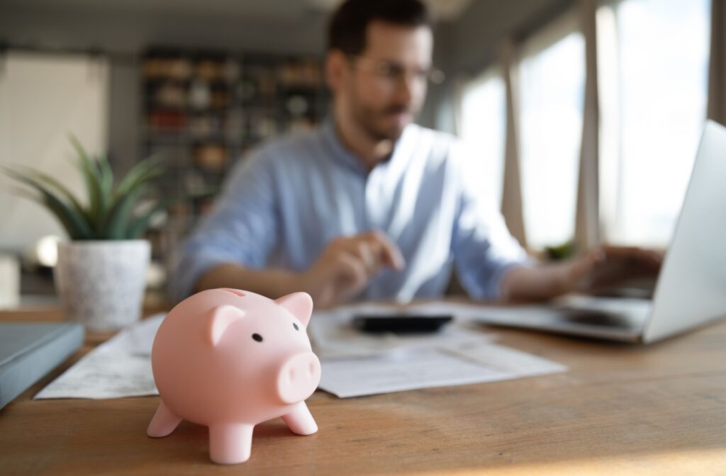 Person doing finances on a laptop with a calculator and papers on their desk, a piggy bank in the foreground.